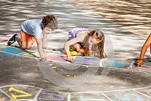 Two kids draw outside in chalk hopscotch