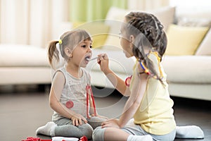 Two kids girls playing doctor at home. Toddler girl opens her mouth and says aaah. Child girl examining little sister.