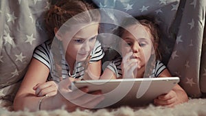 two kids girls under the blanket with a digital tablet. kid dream online video games at concept. daughters kids watching