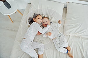 Two kids have fun while liyng down on bed. Interior and design of beautiful modern bedroom at daytime