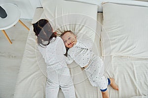 Two kids have fun while liyng down on bed. Interior and design of beautiful modern bedroom at daytime