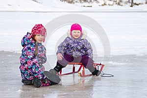 Two kids have fun sitting together on the ice and playing with a snow sled on clear winter day