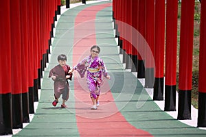 Two kids in kimono walking into at the shrine red gate, in Japanese garden