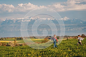 Two kids, little brother and big sister, playing together outdoors in swiss fields with view on lake Geneva