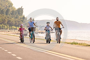 Two kids with parents riding bikes along a sea coastline, front view