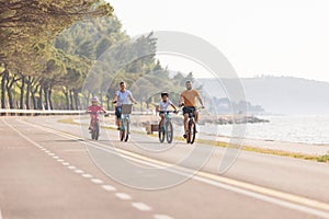 Two kids with parents riding bikes along a sea coastline, front view