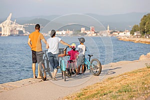 Two kids with parents riding bikes along a sea coastline, front view