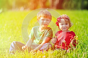Two kids playing with dandelions on green grass
