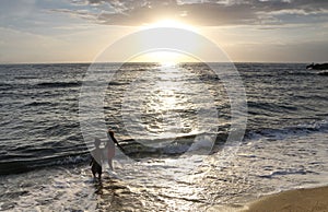 Two kids playing at the shoreline during sunset