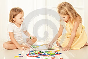 Two kids playing with wooden mosaic in their room