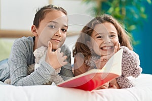 Two kids reading story book lying on bed at bedroom