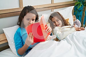 Two kids reading story book sitting on bed at bedroom