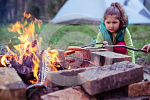 Two kids roasting sausages camp fire.