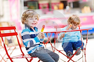 Two kids - sibling boys eating colorful ice cream in summer