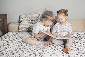 Two kids sitting on bed and reading a book