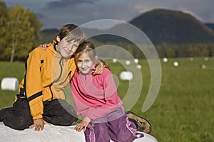 Two kids sitting on a hay bale