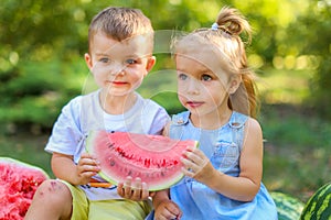 Two kids sitting between watermelons in the garden. Kids eat fruit outdoors. Healthy snack for children. 2 years old