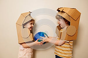 Two kids smile holding a globe in cardboard astronaut helmets