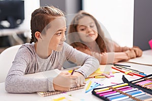 Two kids students sitting on table drawing on notebook paper at classroom