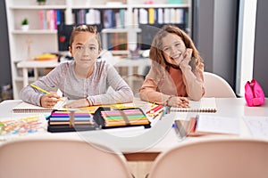 Two kids students sitting on table drawing on notebook paper at classroom
