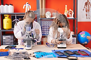 Two kids students using microscopes standing at laboratory classroom