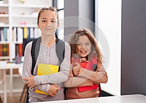 Two kids students wearing backpack holding book at classroom