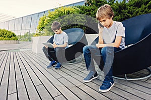 Two kids with tablet and smart phone in the city outdoors.