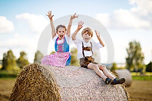 Two kids, boy and girl in traditional Bavarian costumes in wheat field with hay bales