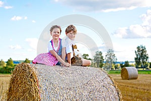 Two kids, boy and girl in traditional Bavarian costumes in wheat field with hay bales