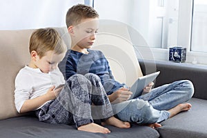 Two kids using tablet pc and smartphon at home. Brothers with tablet computer in light room. Boys playing games on tablet computer