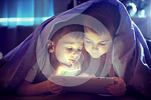 Two kids using tablet pc under blanket