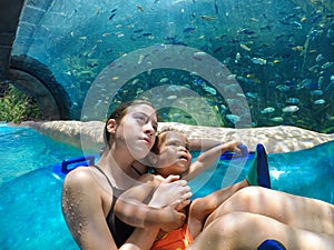 Two kids on a water ride through with a large aquarium