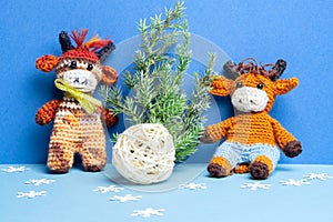 Two knitted bull toys with Christmas tree, ball and snowflakes on blue background
