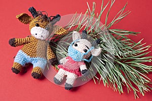 Two knitted bull toys on a red background. The cow toy is wearing a protective face mask.