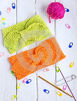 Two knitted headbands for girls: light green, orange, pink. Hair bands are on a white wooden background with hooks.