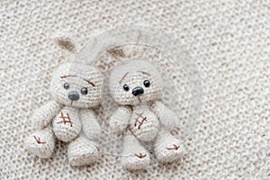 Two knitted white hares are lying on a light knitted handmade fabric photo