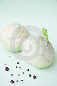 Two kohlrabies with some peppercorns and allspice on a paper background.