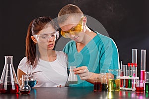 Two lab technicians are examining a flask with a green liquid that the guy is holding in his hand.