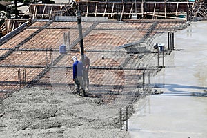 two labor work pouring liquid concrete from cement mixer to building floor in construction site