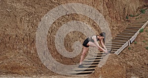 Two ladies in a black sportswear stretching legs on the wooden stents beside the beach background big rocks