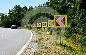 Two lane asphalt road with sharp curve. direction arrows traffic signs.