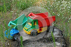 Two large colored toys dump trucks standing on a stump