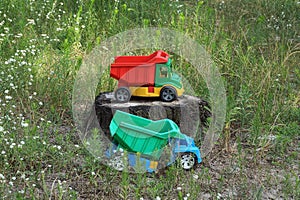 Two large colored toys dump trucks standing on a stump