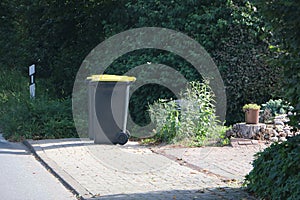 two Large, dark plastic garbage cans with yellow lids sit on the side of the road ready for collection