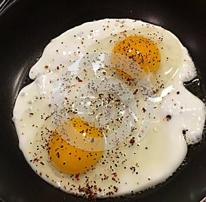 Two large eggs sprinkled with black pepper.
