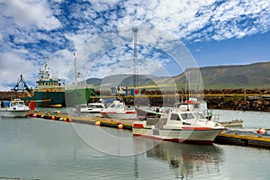 Two large fishing boats and many small boats moored at the harbor in the Icelandic countryside