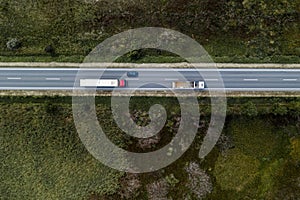 Two large freight transporter semi-trucks and a car on the road, aerial view