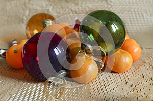 Two large glass Christmas tree balls lie on a pile of tangerines.Macro