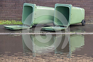Two large green rubbish bins, lying in UK street, with large puddle, floodwater. After storm photo