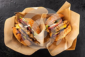 Two large grilled chicken burgers in a craft box on a dark background, top view.